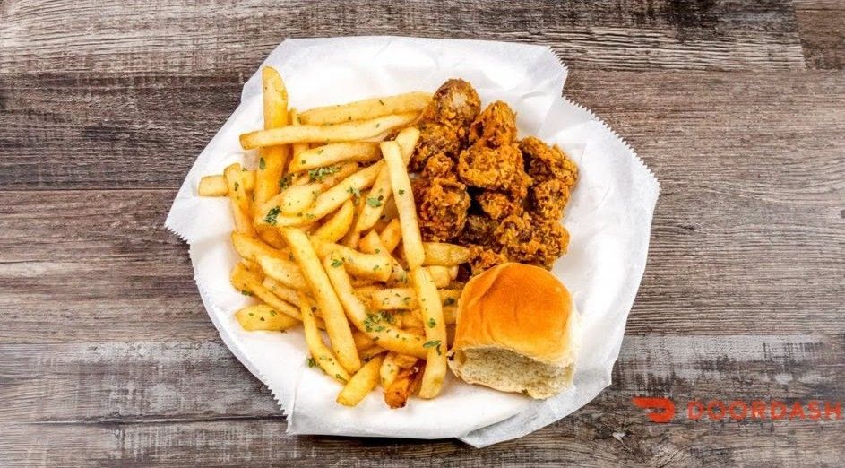Fried chicken, fries, and a sandwich on white paper-lined tray over a wooden table.