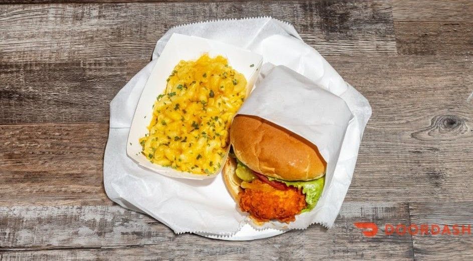 Burger and yellow rice in a white takeout container on a plate on a wooden table