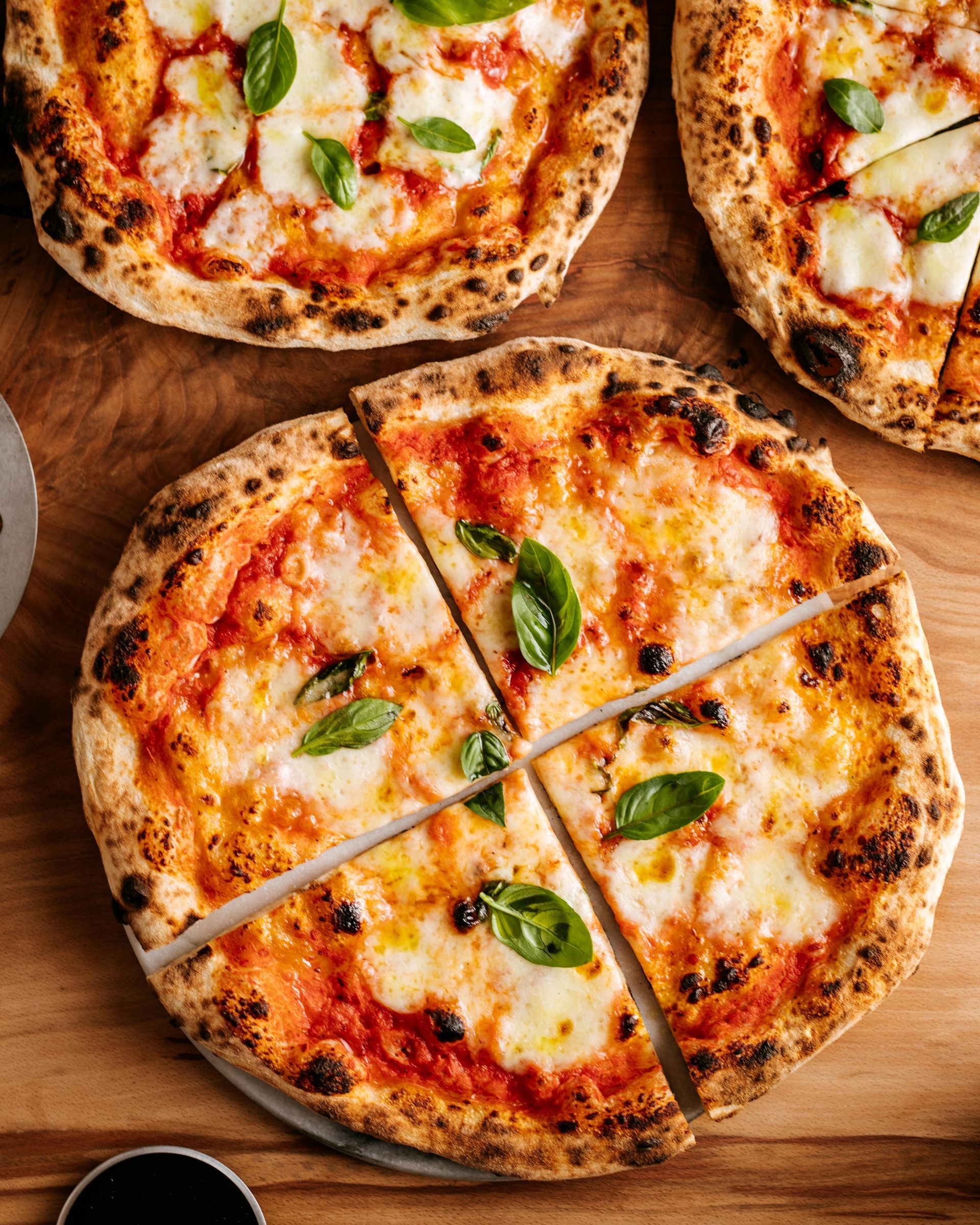 Three pizzas are sitting on top of a wooden table.