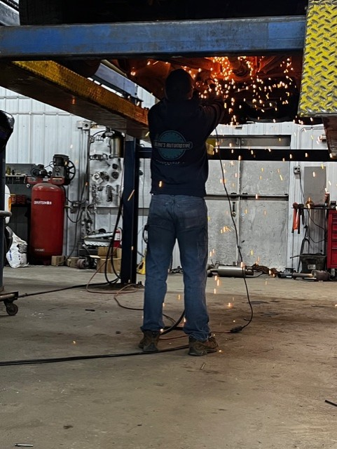 Mechanic working under a car on a hydraulic lift in a garage, using a wrench.