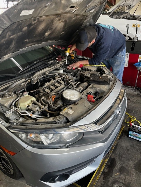 Person pouring oil from a bottle into a car engine; auto repair shop.
