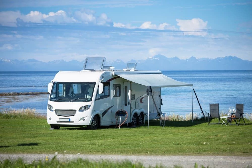 A RV is Parked in a Grassy Field Next to the Ocean — Lake Macquarie Caravan Repairs In Cardiff, NSW