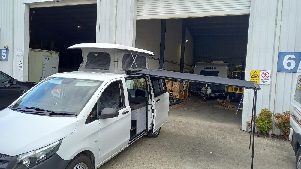 A White Van With A Pop Top Roof Is Parked In Front Of A Garage — Lake Macquarie Caravan Repairs In Gosford, NSW