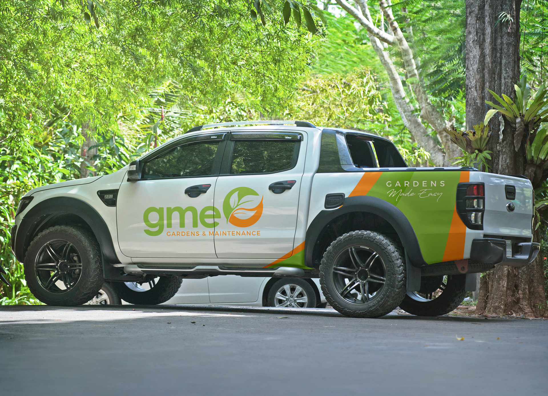White SUV with green and orange GME branding parked beside a tree on a leafy road
