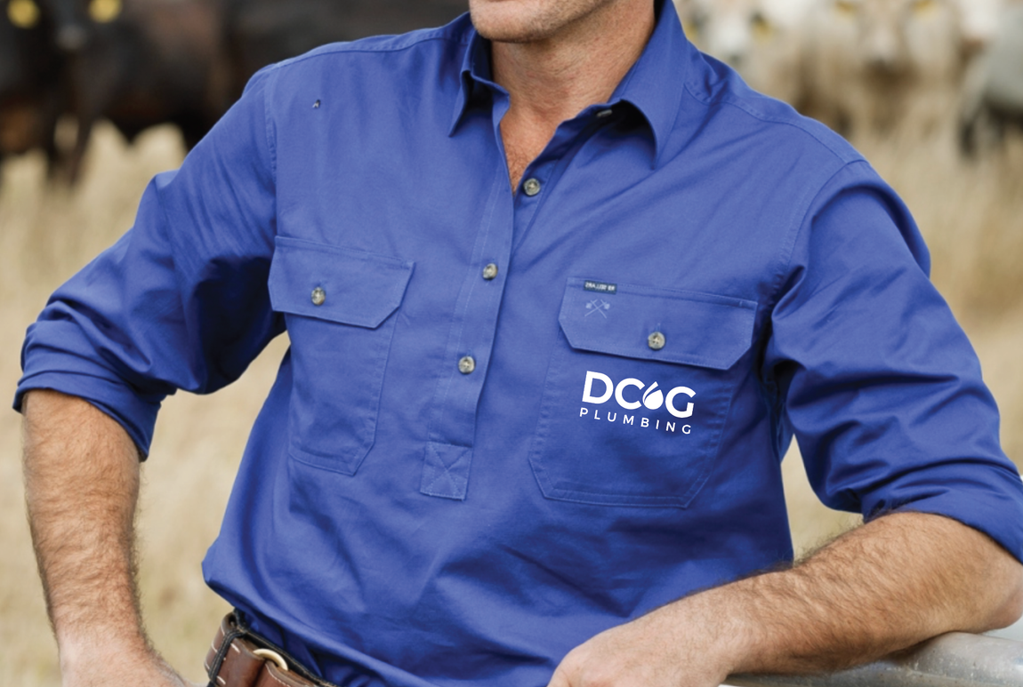 Man wearing a blue work shirt with logo, leaning on a fence, cows in background.
