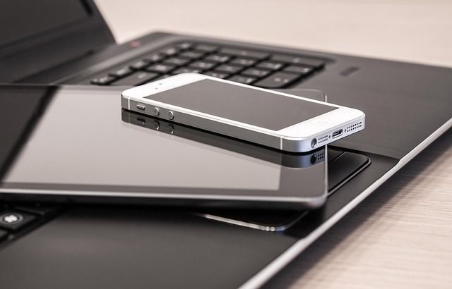 Smartphone resting on a closed laptop on a desk, with another laptop keyboard in the background.