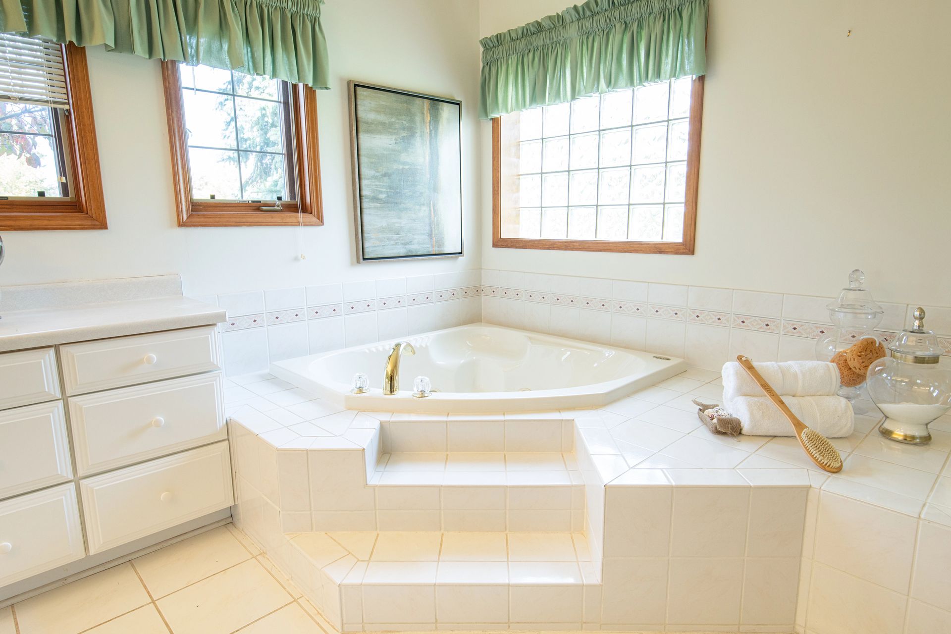 White bathroom with corner jacuzzi tub, windows, and vanity. Green curtains.