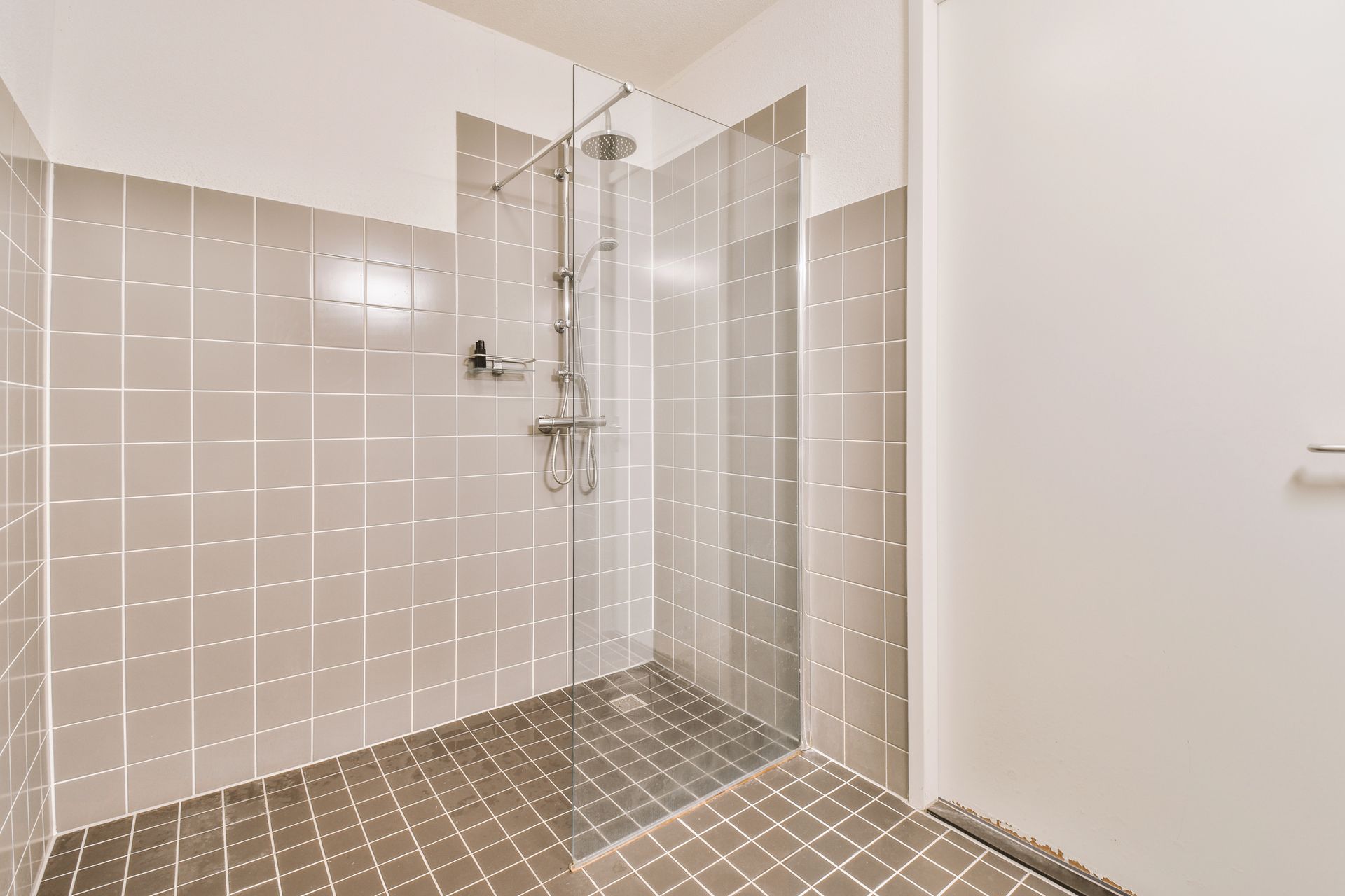 A walk-in shower with gray tiled walls and floor, silver shower fixtures, and a glass partition.