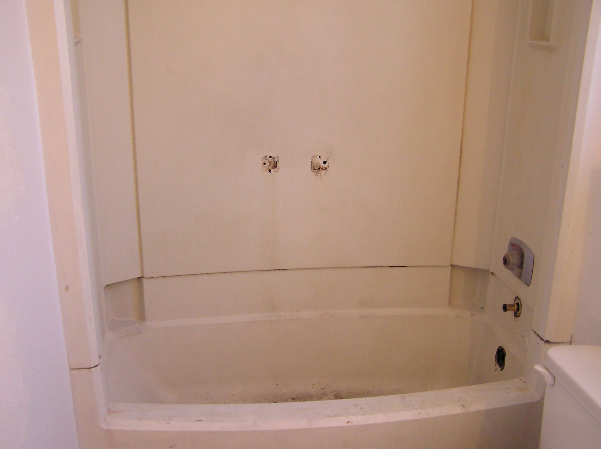 White, empty bathtub with exposed pipes in a tiled alcove, ready for renovation.