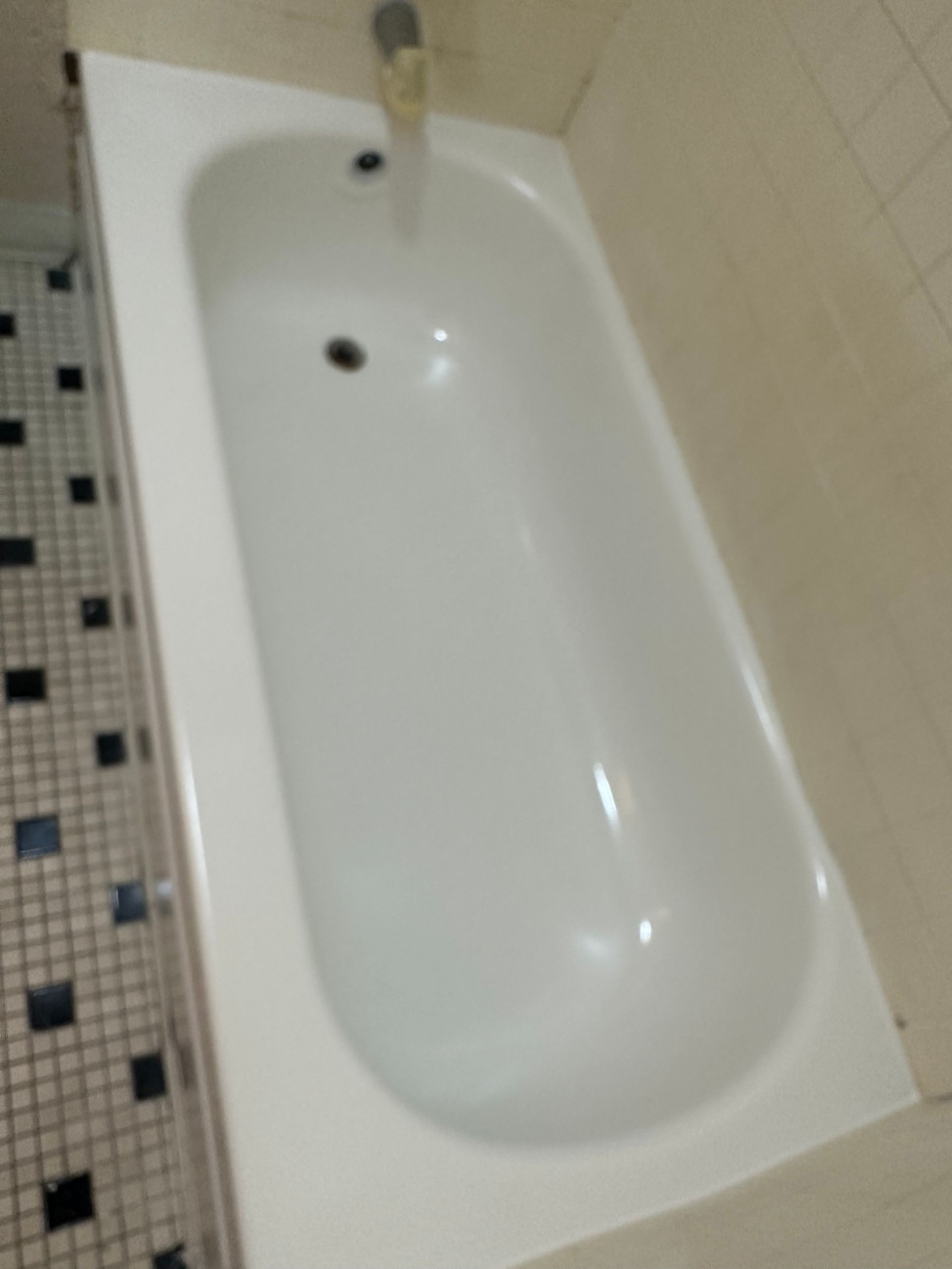 White bathtub in a tiled bathroom, viewed from above. Black and white tiles on the floor.