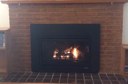 after of a fireplace in a living room with a brick wall and a wooden mantle 