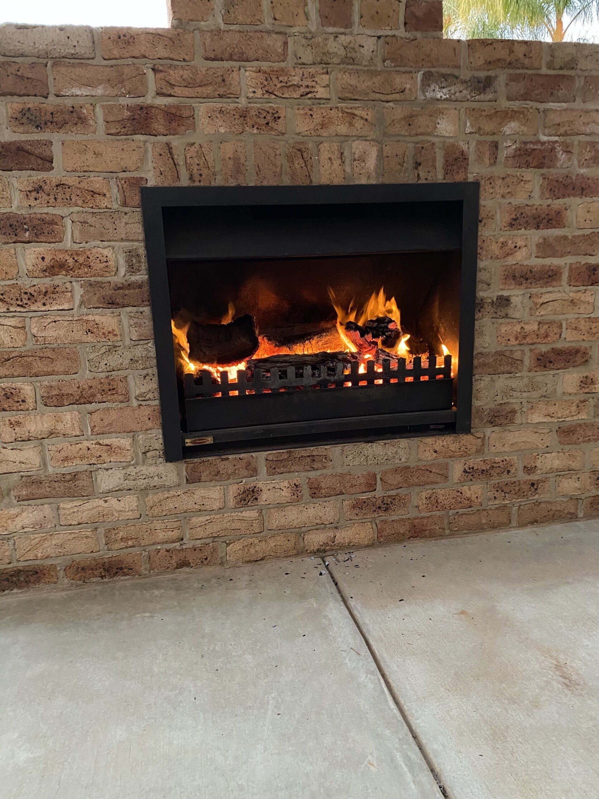 fireplace built into exterior brick wall with view of tree in backdground
