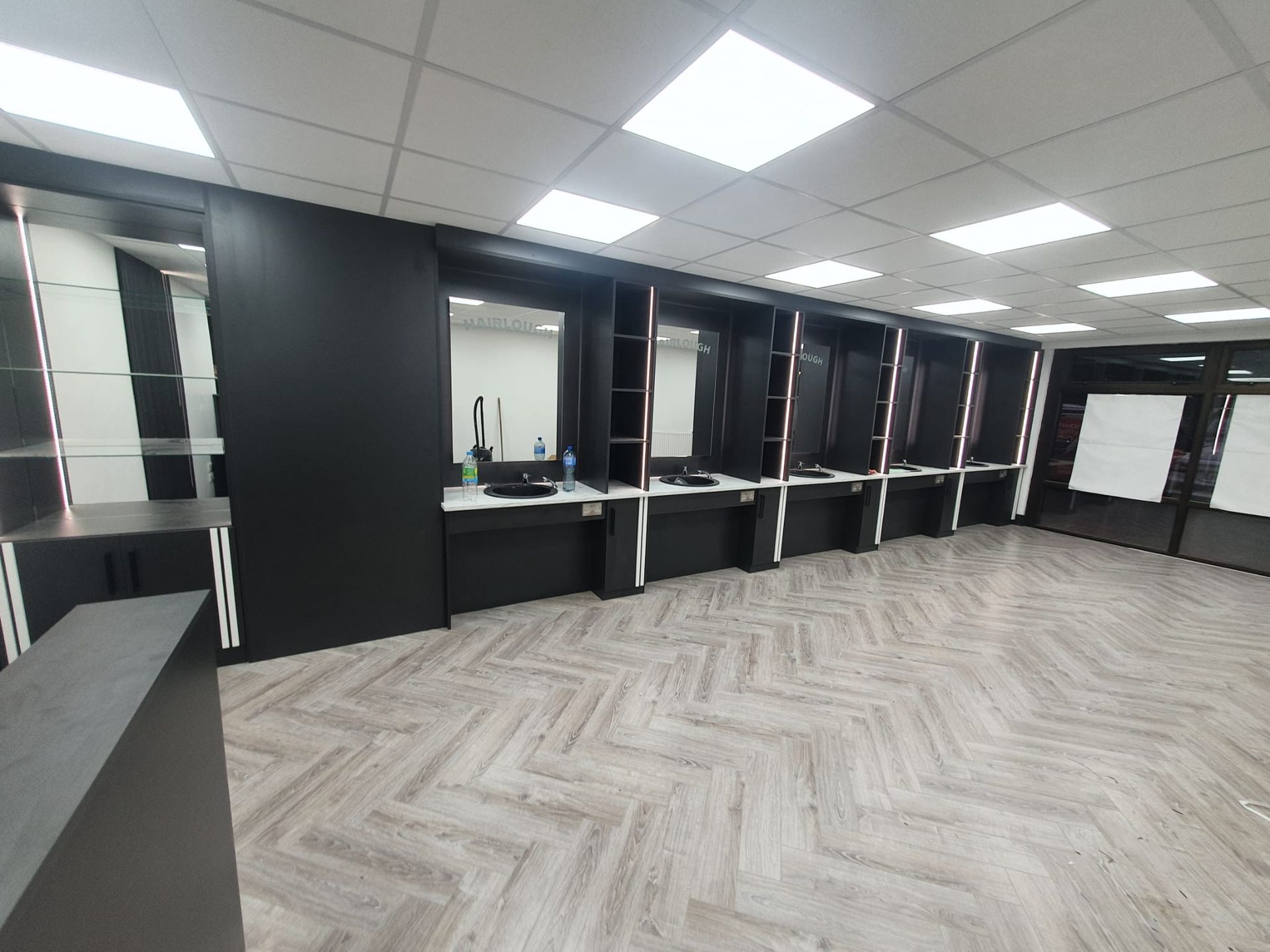 A large empty room with a herringbone floor and a row of desks.