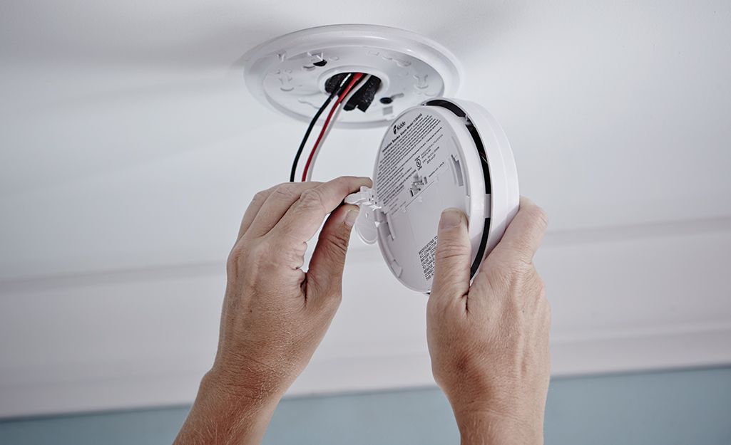 A person is installing a smoke detector on the ceiling.