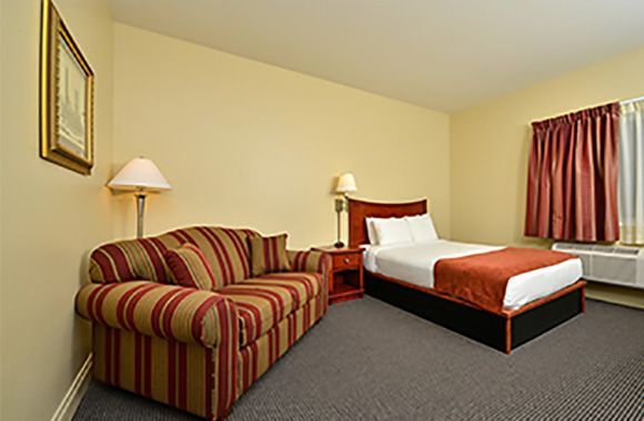 Hotel room with a striped sofa, bed, lamps, and red curtains on beige walls