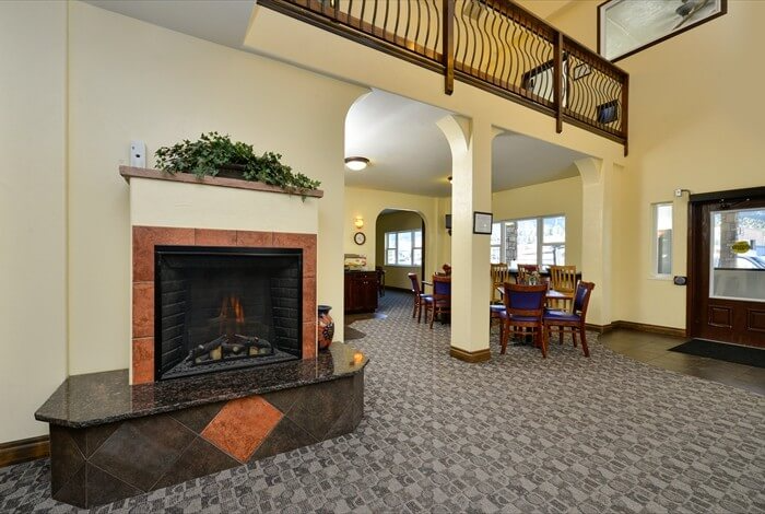 Spacious lobby with fireplace, carpeted floor, and dining area under a balcony.