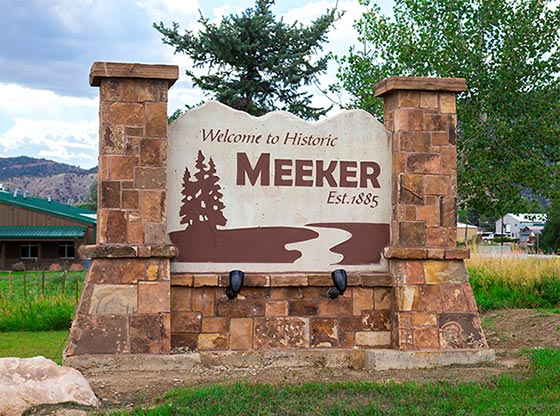 Welcome sign for Meeker, Est. 1885, on a stone monument with pine tree and bear silhouettes.