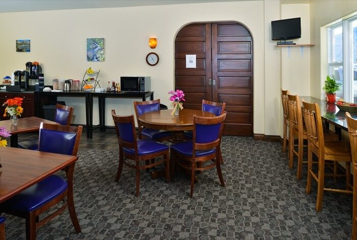 Dining room with wooden tables and chairs, a serving counter, and a double door in the background.