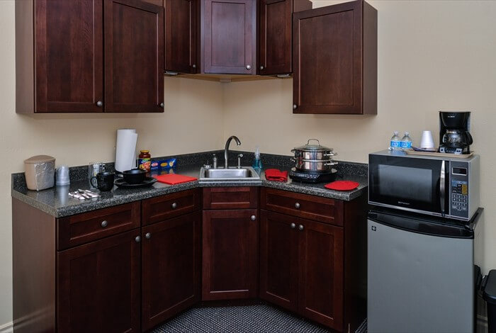 Compact kitchen with dark wood cabinets, black countertops, and a microwave on a small refrigerator.