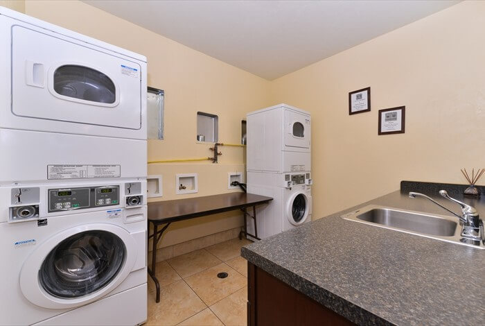 Laundry room with stacked washer-dryers, a countertop sink, and beige walls