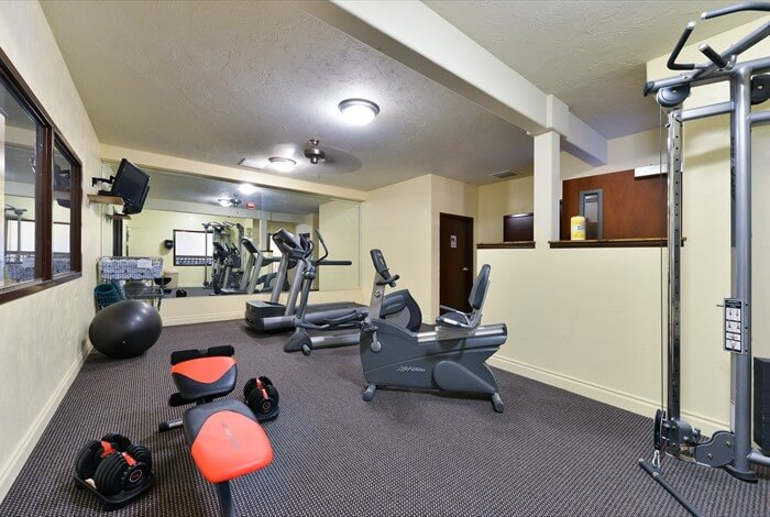 Gym with exercise equipment, including treadmills, weights, and a cable machine, in a carpeted room.
