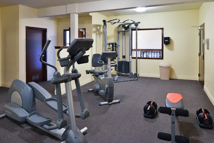 Small gym room with exercise bikes, elliptical machine, dumbbells, and a stability ball