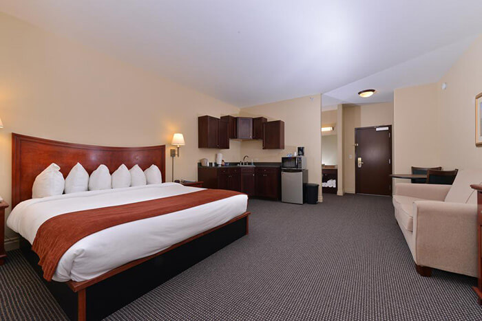 Hotel room with a large bed, desk, kitchenette, and sofa in a beige interior