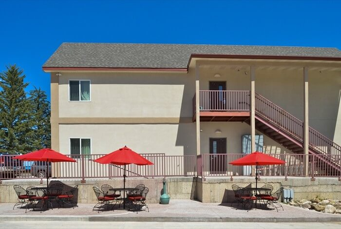 Motel exterior with beige walls, red patio umbrellas, and outdoor tables under a blue sky.
