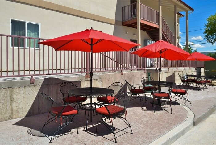 Outdoor patio with red umbrellas and tables beside a building on a sunny day