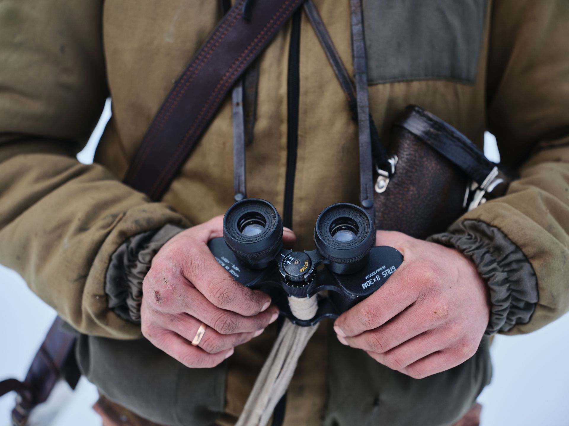 Person holding black binoculars, wearing a brown jacket in an outdoor snowy setting