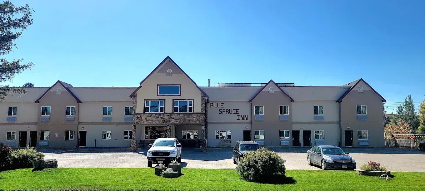 Wide photo of a beige apartment building with parked cars and shrubs in front under a clear blue sky