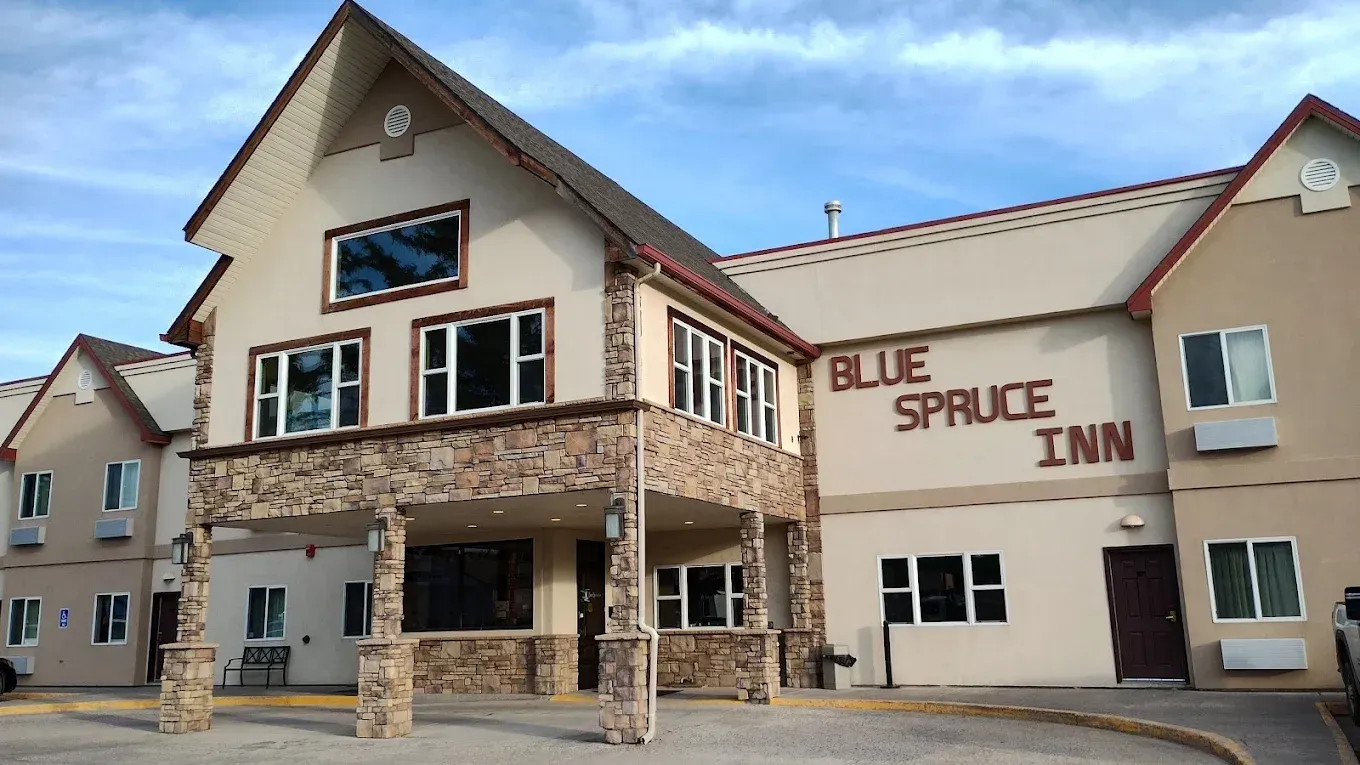 Blue Spruce Inn exterior with beige stone facade and red roof under a cloudy sky
