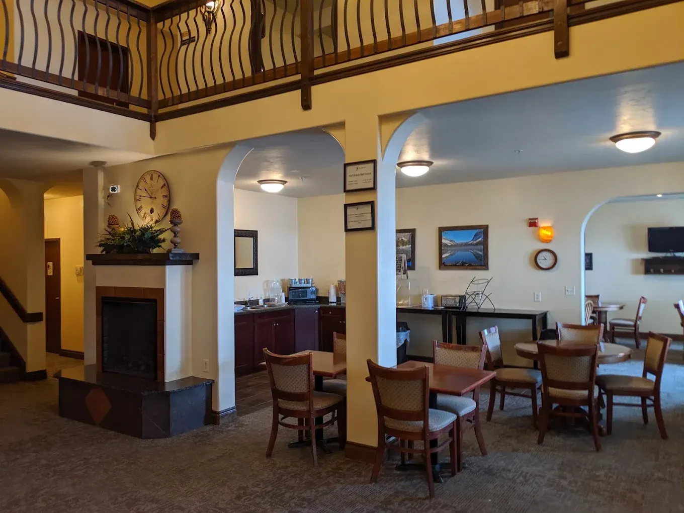 Lobby seating area with tables and chairs, arched doorways, and a balcony railing above