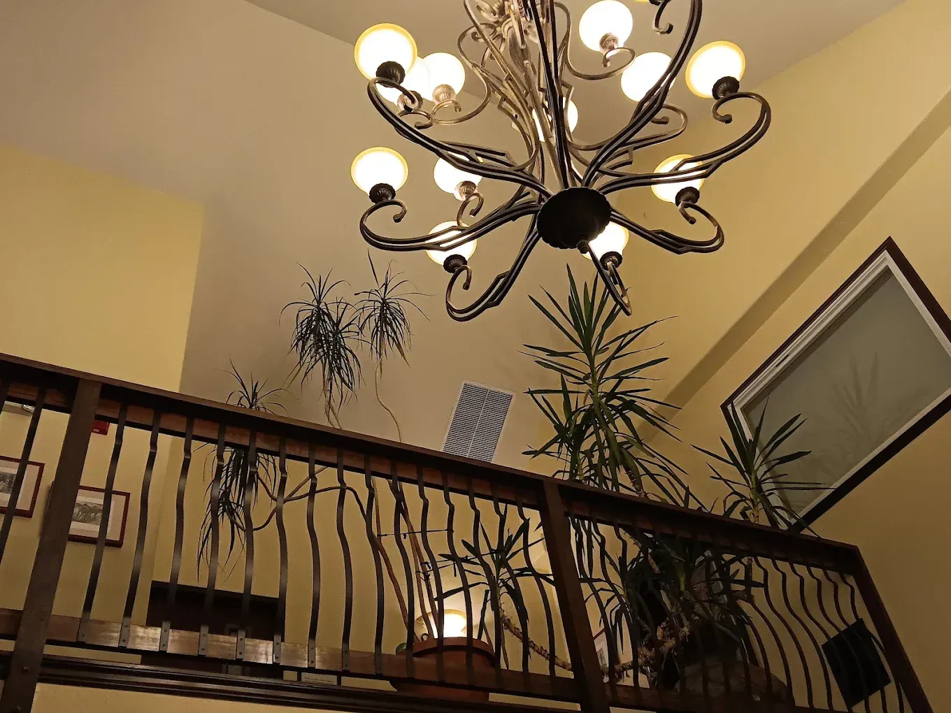 Indoor staircase with wrought-iron railing, potted plants, and a decorative chandelier overhead.