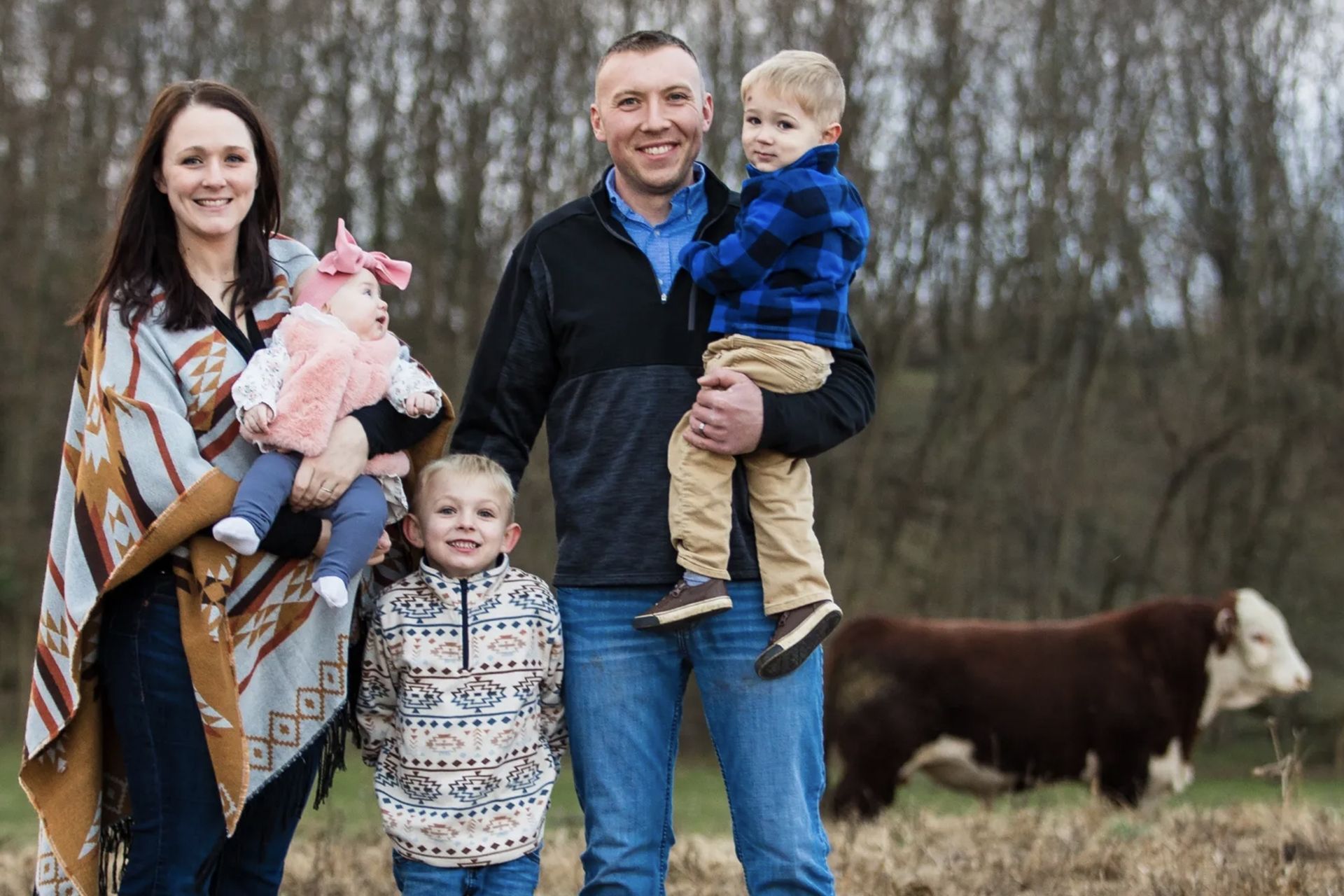 A family is posing for a picture in a field with a cow in the background.