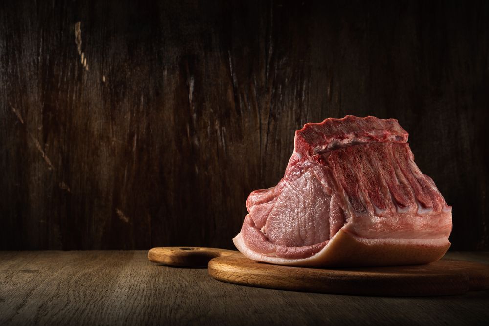 A piece of raw pork is sitting on a wooden cutting board.