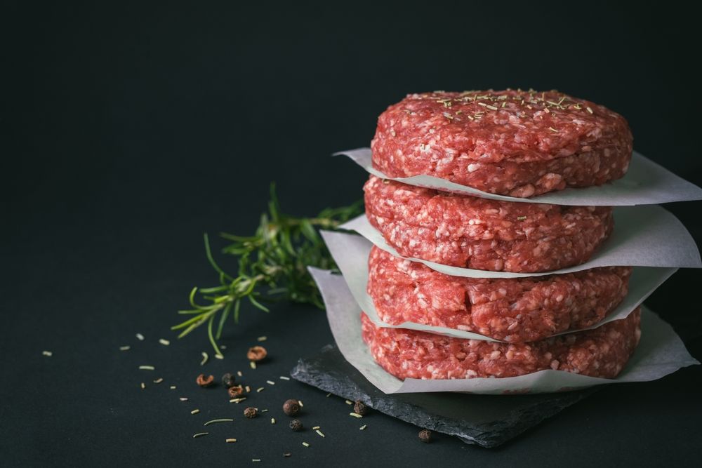 Three raw hamburger patties are stacked on top of each other on wax paper.