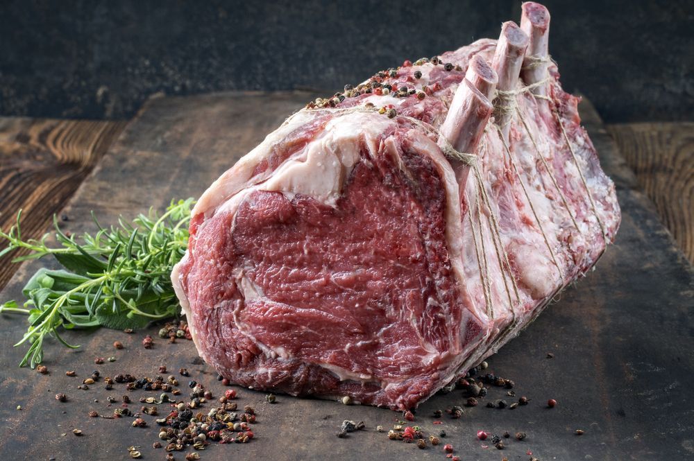 A large piece of raw beef is sitting on a wooden cutting board.