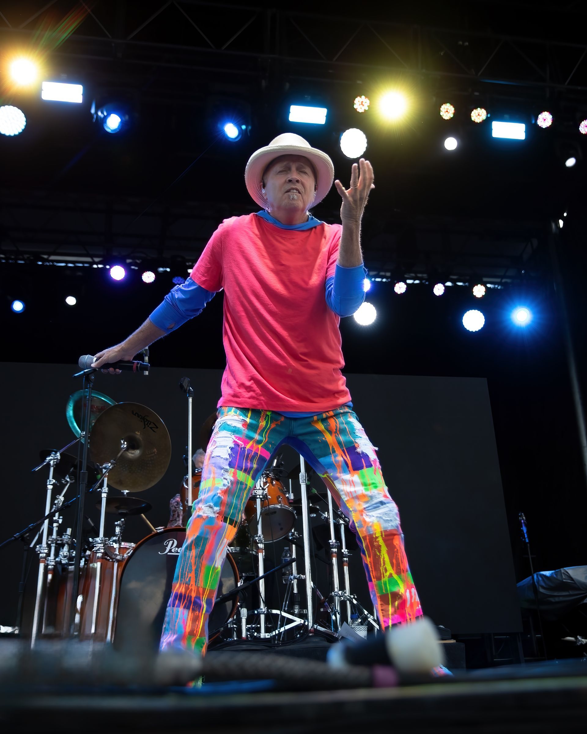 A man in a cowboy hat and colorful pants is singing into a microphone on a stage