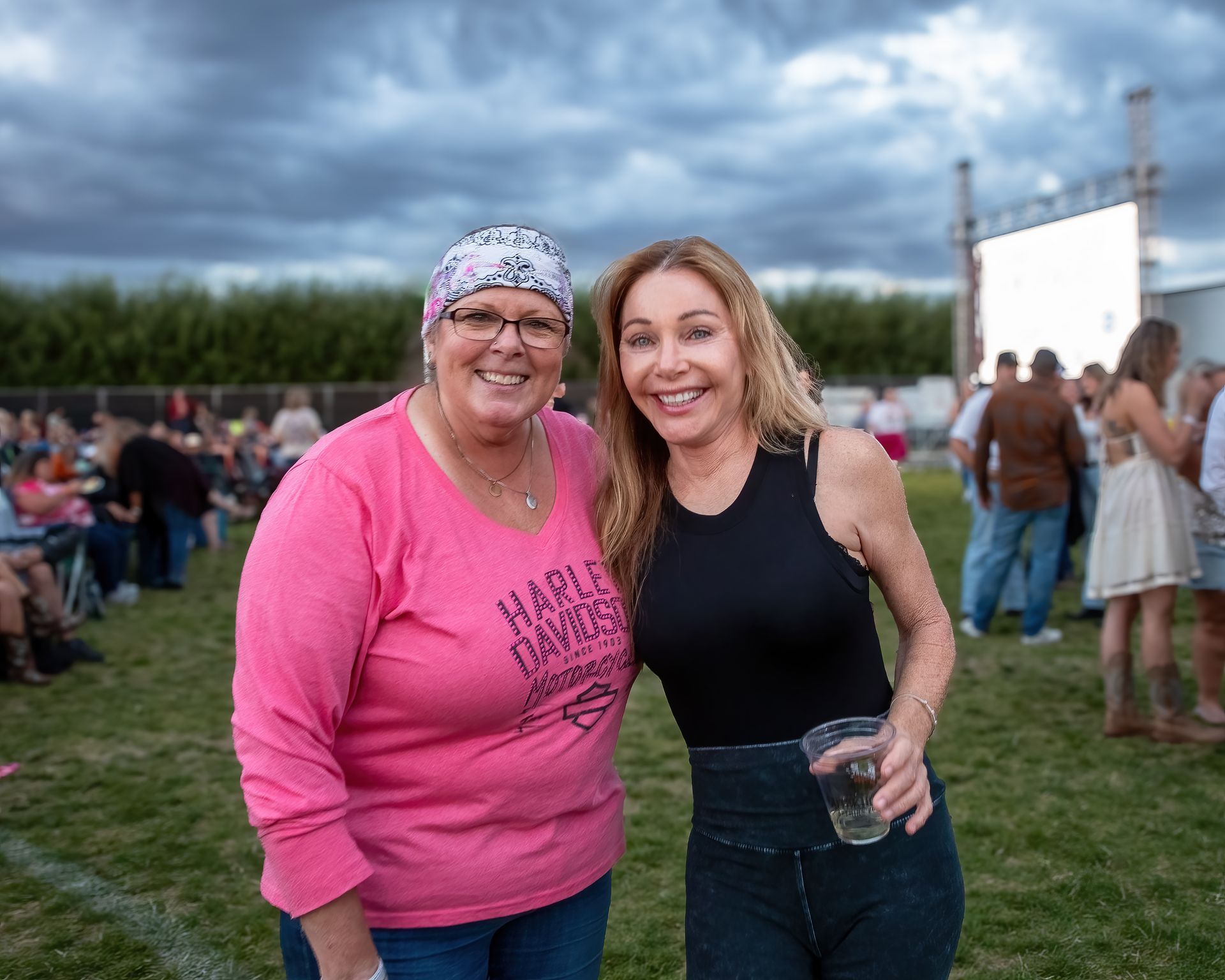 Two women are posing for a picture in a field . one of the women is wearing a pink shirt.
