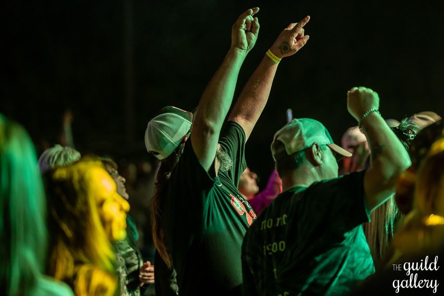 A crowd of people are dancing at a concert with their arms in the air.