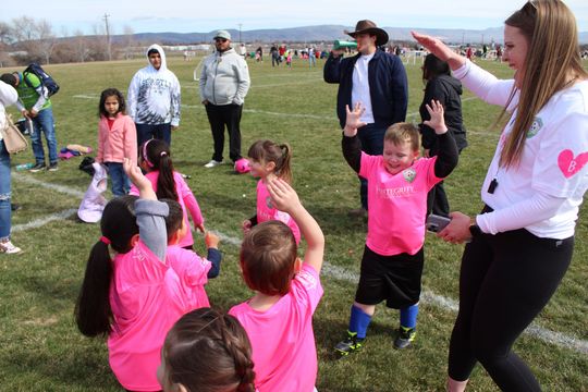 Children in pink shirts stretching outdoors while adults watch in a grassy field