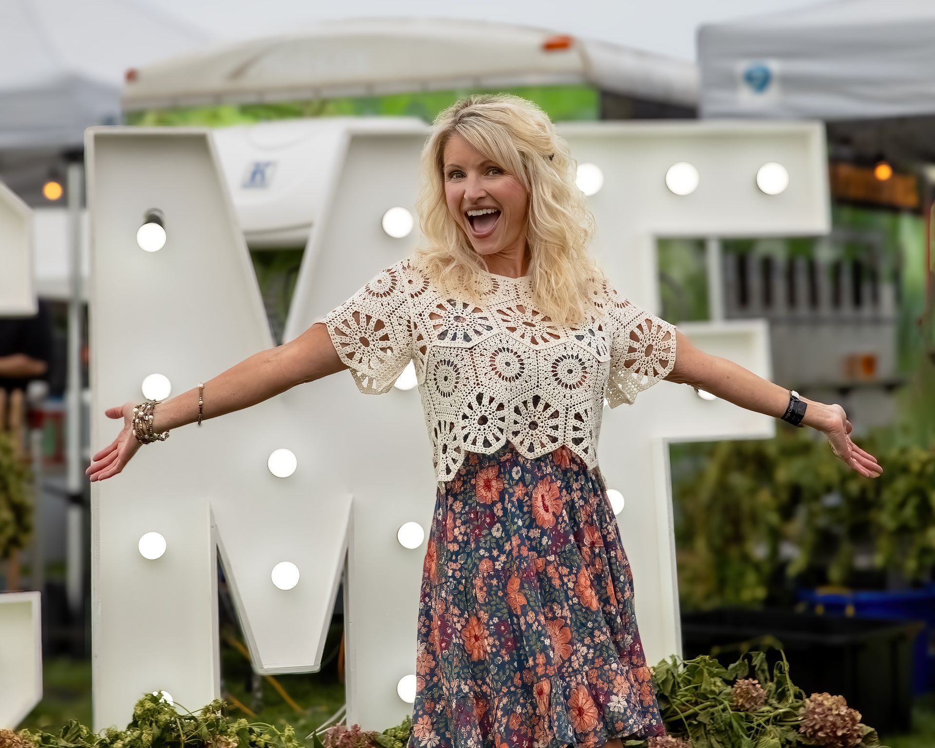 A woman is standing in front of a large letter m with her arms outstretched.