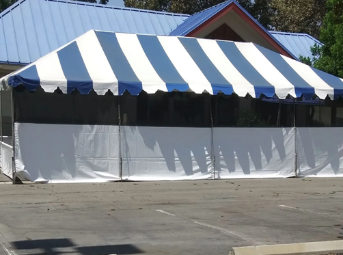 Blue-and-white striped event tent with white side panels on a paved lot
