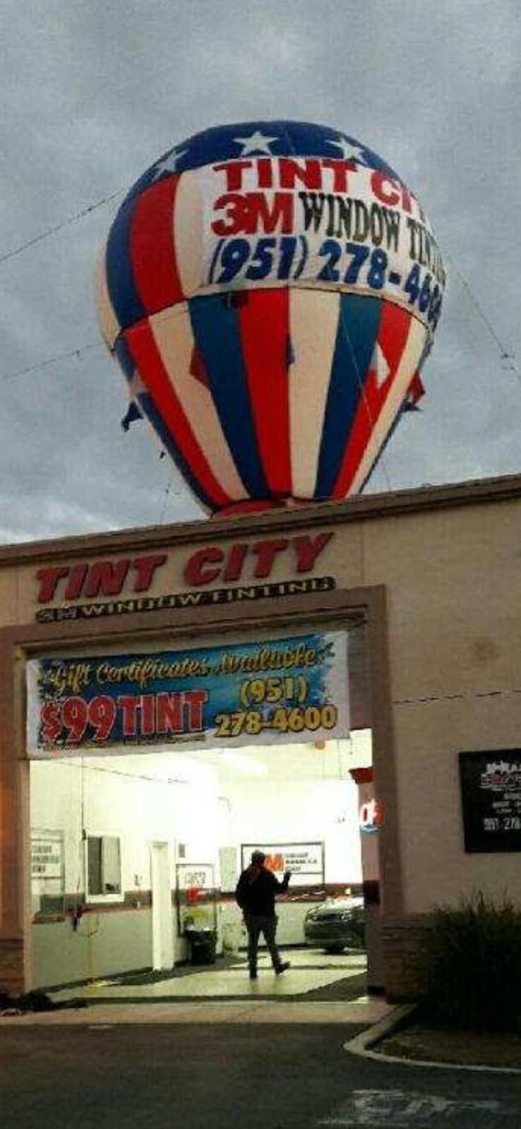 Tint City storefront with a large red, white, and blue balloon sign outside at dusk