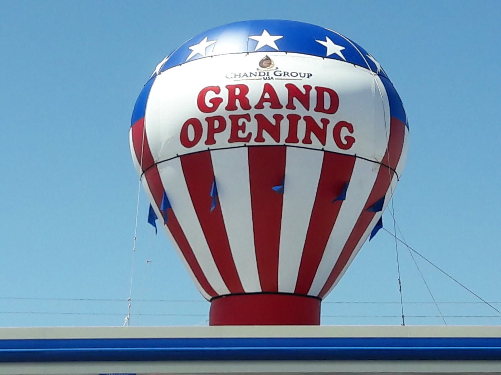 Red, white, and blue hot air balloon with “Grand Opening” text against a clear sky