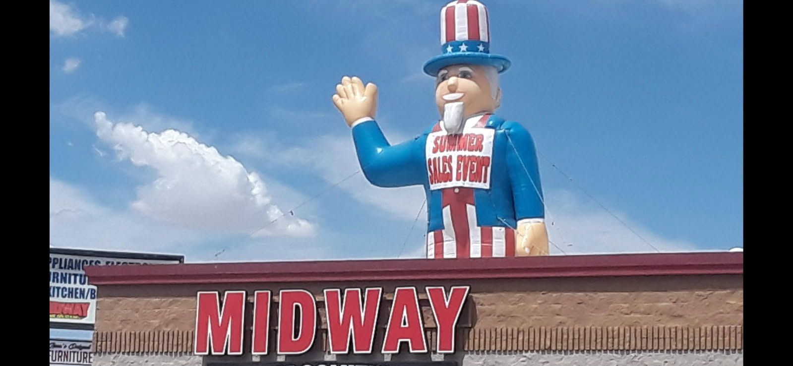 Statue of Uncle Sam waving above a MIDWAY building sign under a blue sky