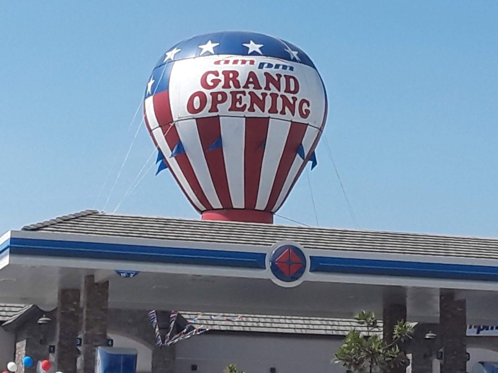 Gas station canopy with a large red, white, and blue “Grand Opening” hot air balloon sign