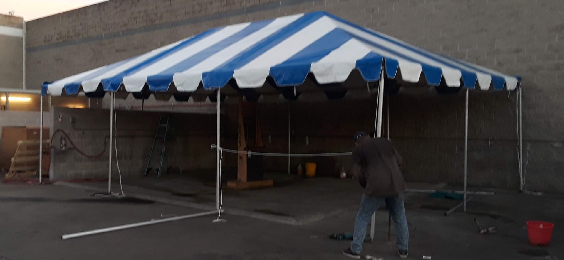Blue-and-white striped event tent set up on a parking lot, with a person working beside it