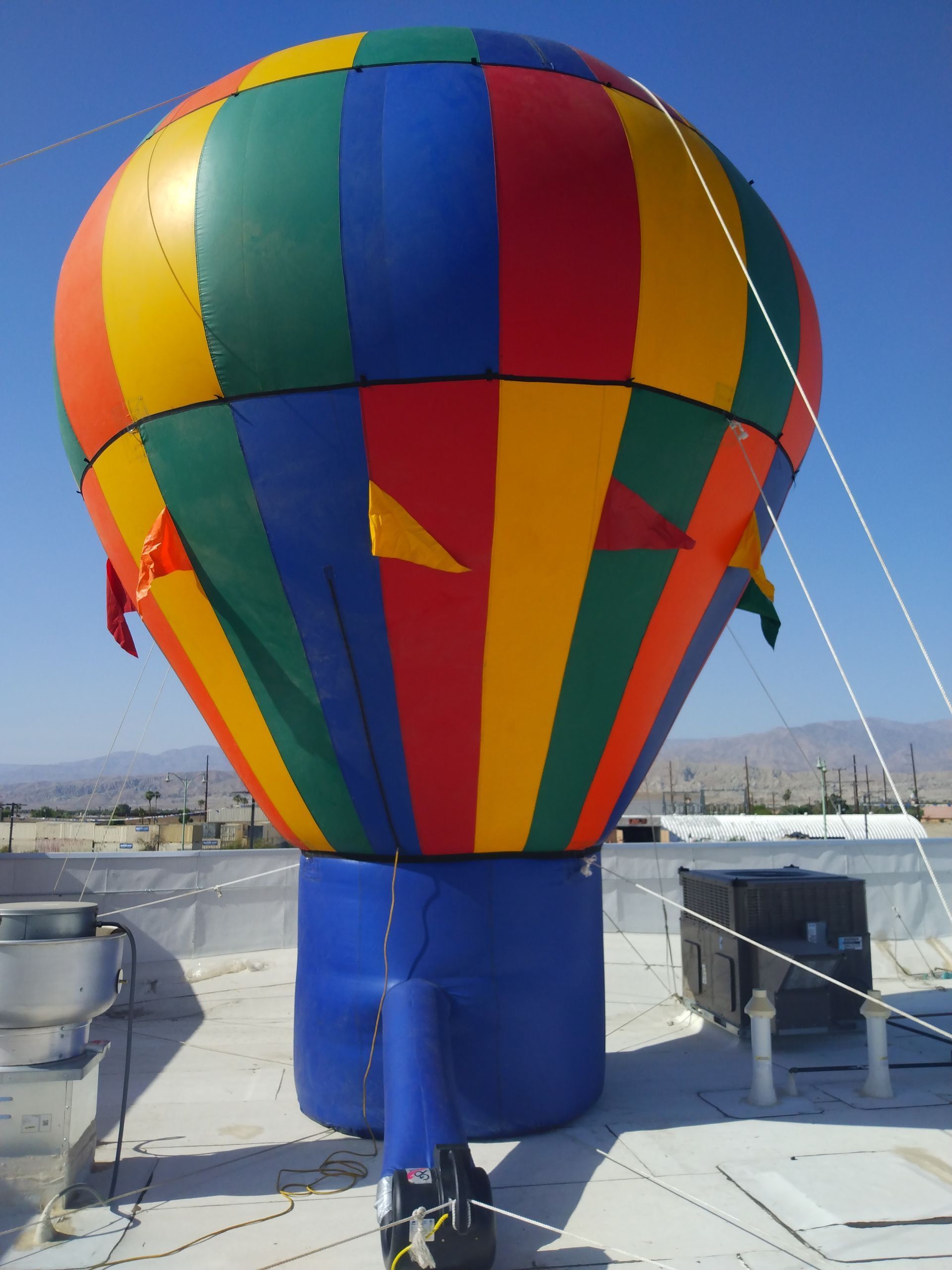 Multicolored hot air balloon inflated on a rooftop under a clear blue sky